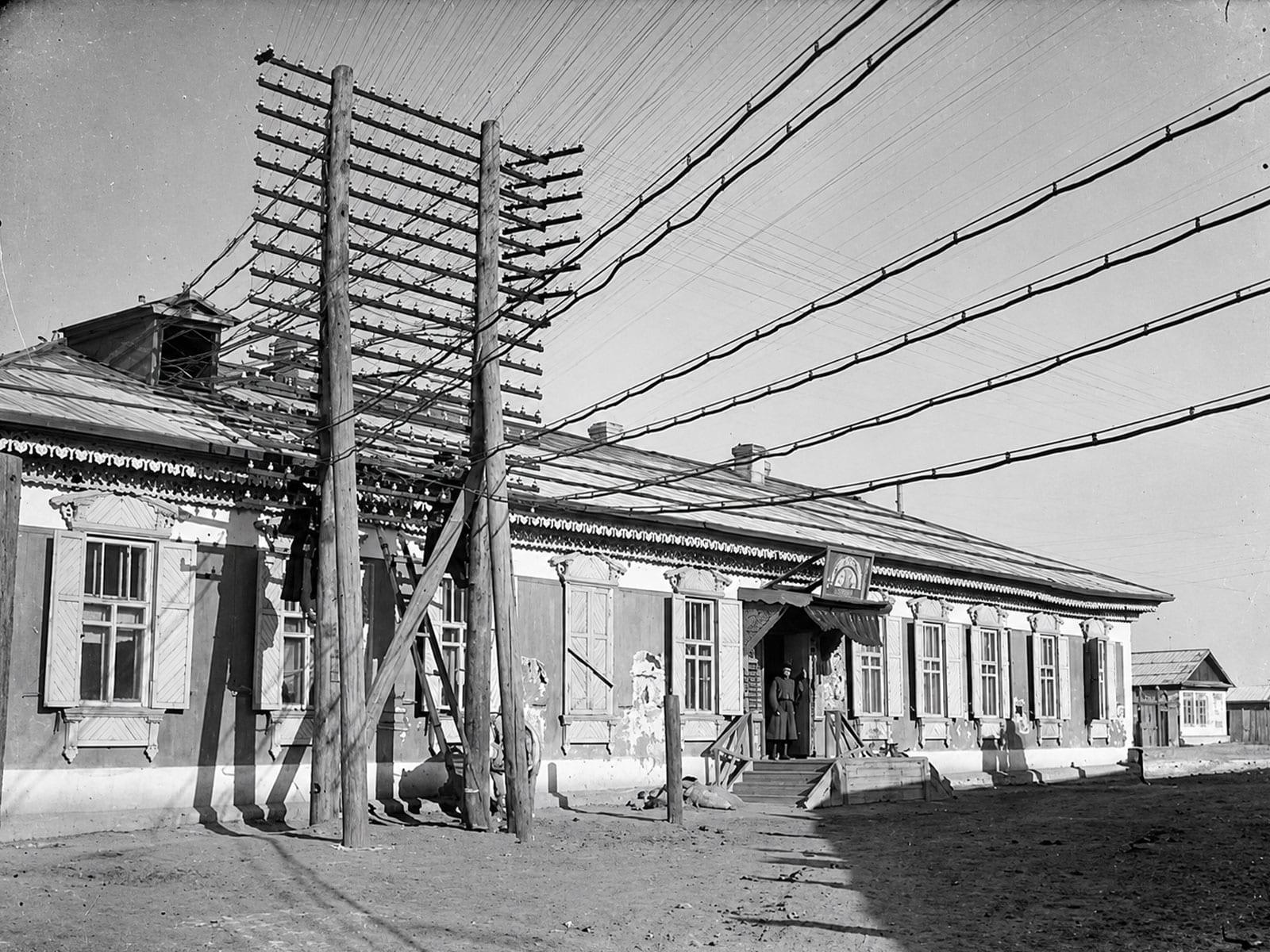 Telegraph poles and lines in front of an ornate wooden building.