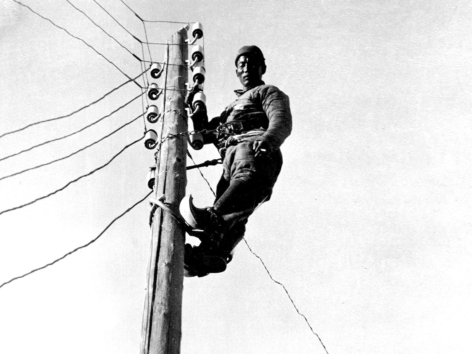 A linesman working on telephone lines from a wooden pole.