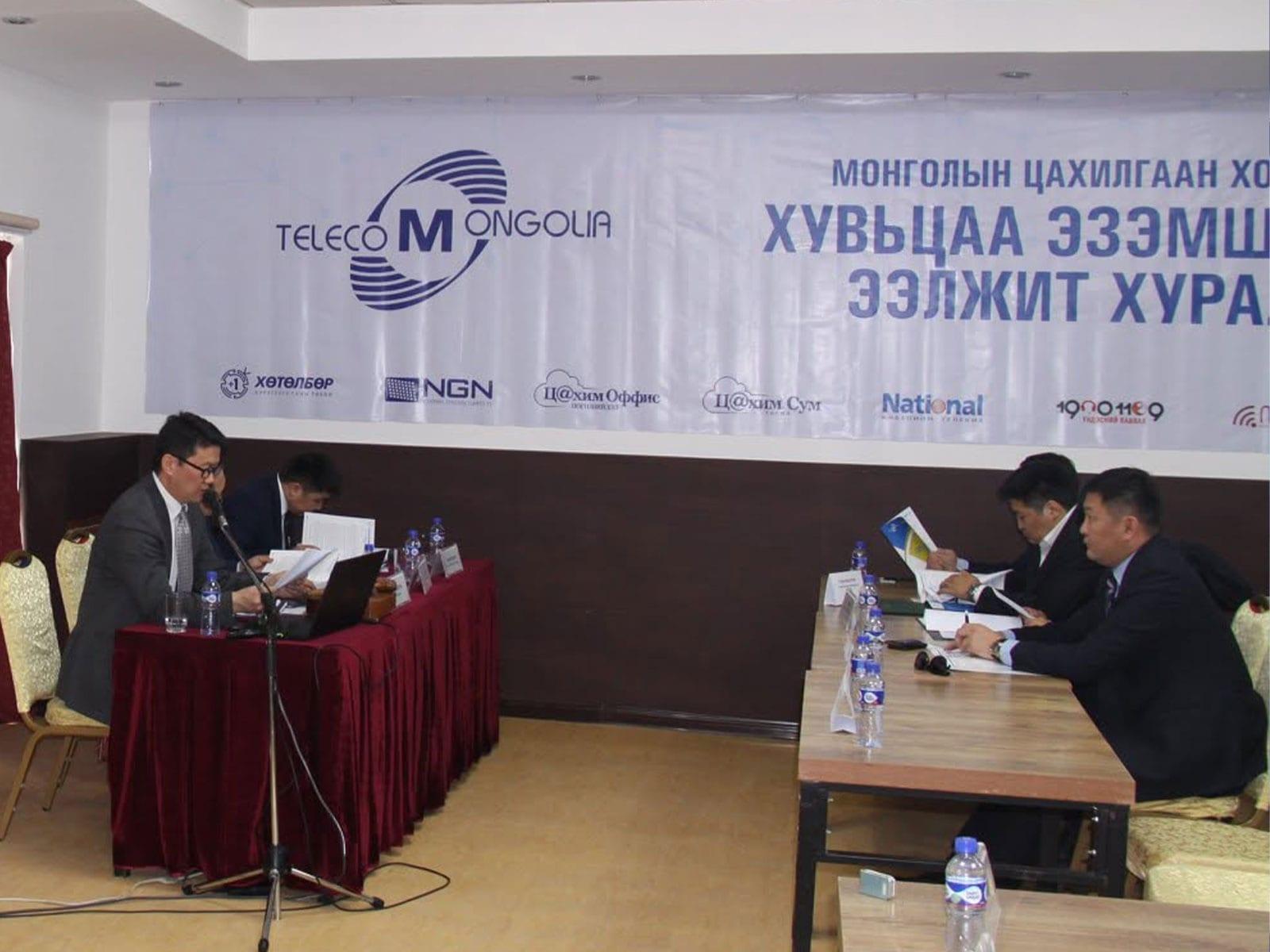 People seated at a shareholders meeting beneath a Telecom Mongolia banner.