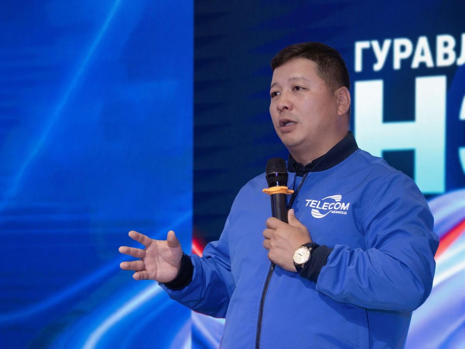 A speaker in a Telecom Mongolia jacket holding a microphone.
